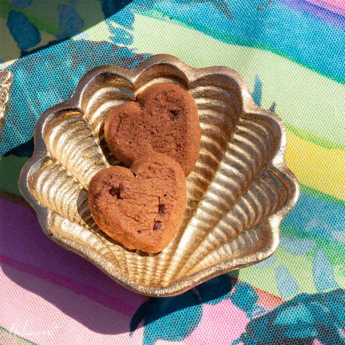 Goudkleurige keramieken schaal in de vorm van een schelp gevuld met koekjes.